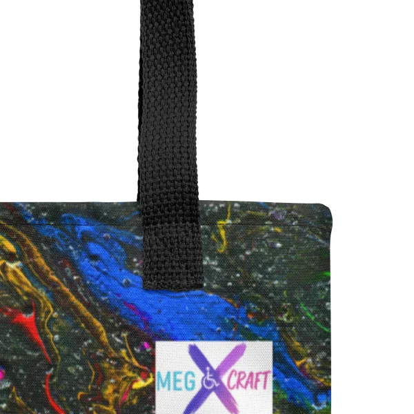 Close up of the tote bag showing the black handle and stitching with bright swirls of red, blue, and yellow mix with green representing the main characters on a glittering charcoal background to invoke the feel of space.