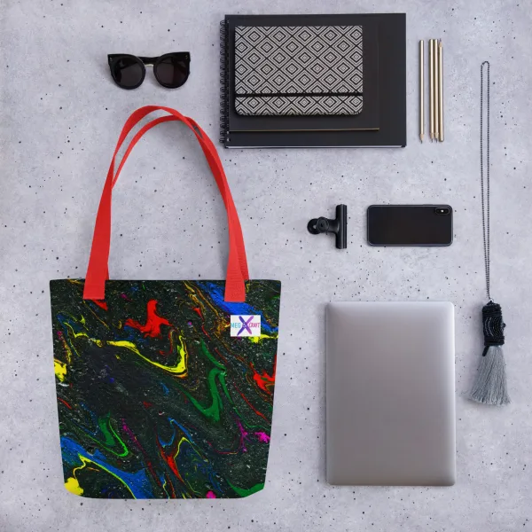 Tote bag with bright swirls of red, blue, and yellow mix with green representing the main characters on a glittering charcoal background to invoke the feel of space and red handles surrounded by accessories like sunglasses and a laptop demonstrating what can go into the bag.
