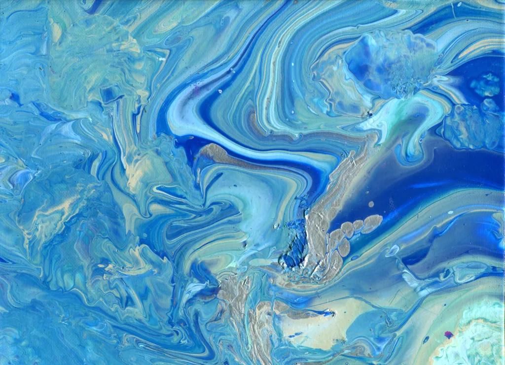 Shades of blue swirl in eddies and currents around the sandy shores of land and gold with dark blues marking the edge falling into cavernous deeps alongside splashes of white ocean spray along the Ocean's Surface.